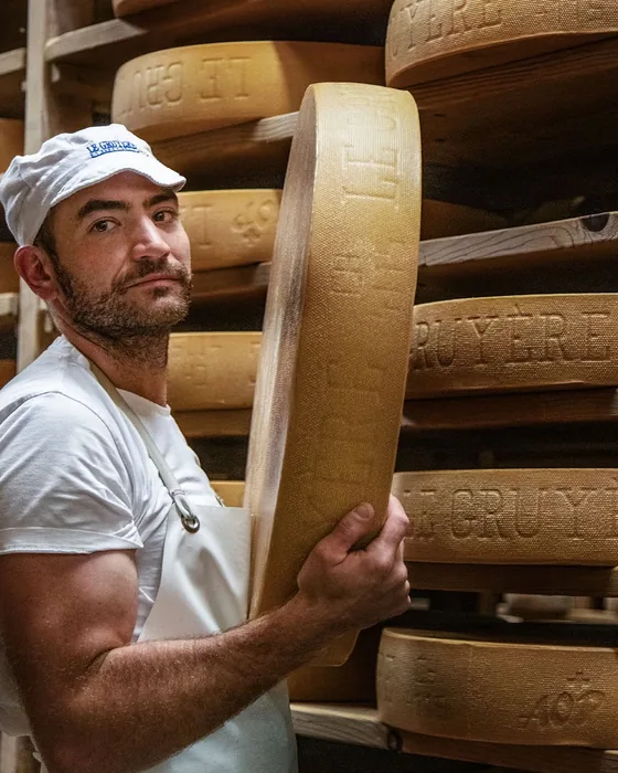 Un producteur dans sa cave d’affinage, une meule de fromage à la main
